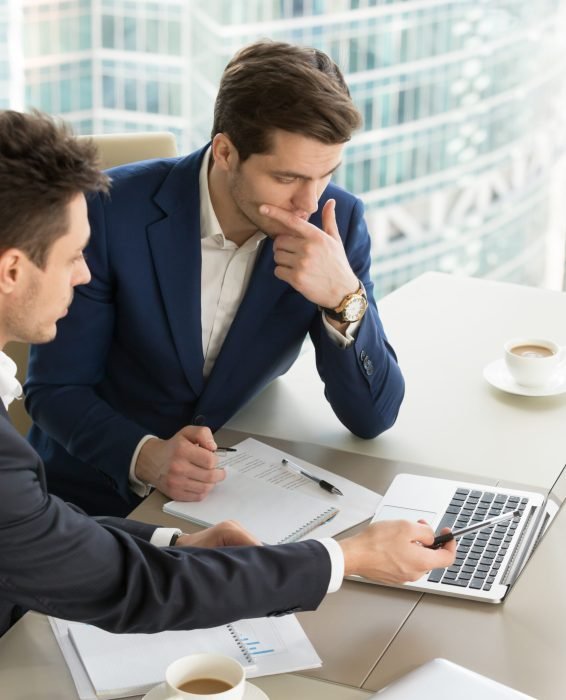 Business partners using laptop while working together on important corporate project in office. Businessman attentively listening to adviser Investment specialist making presentation of promising deal